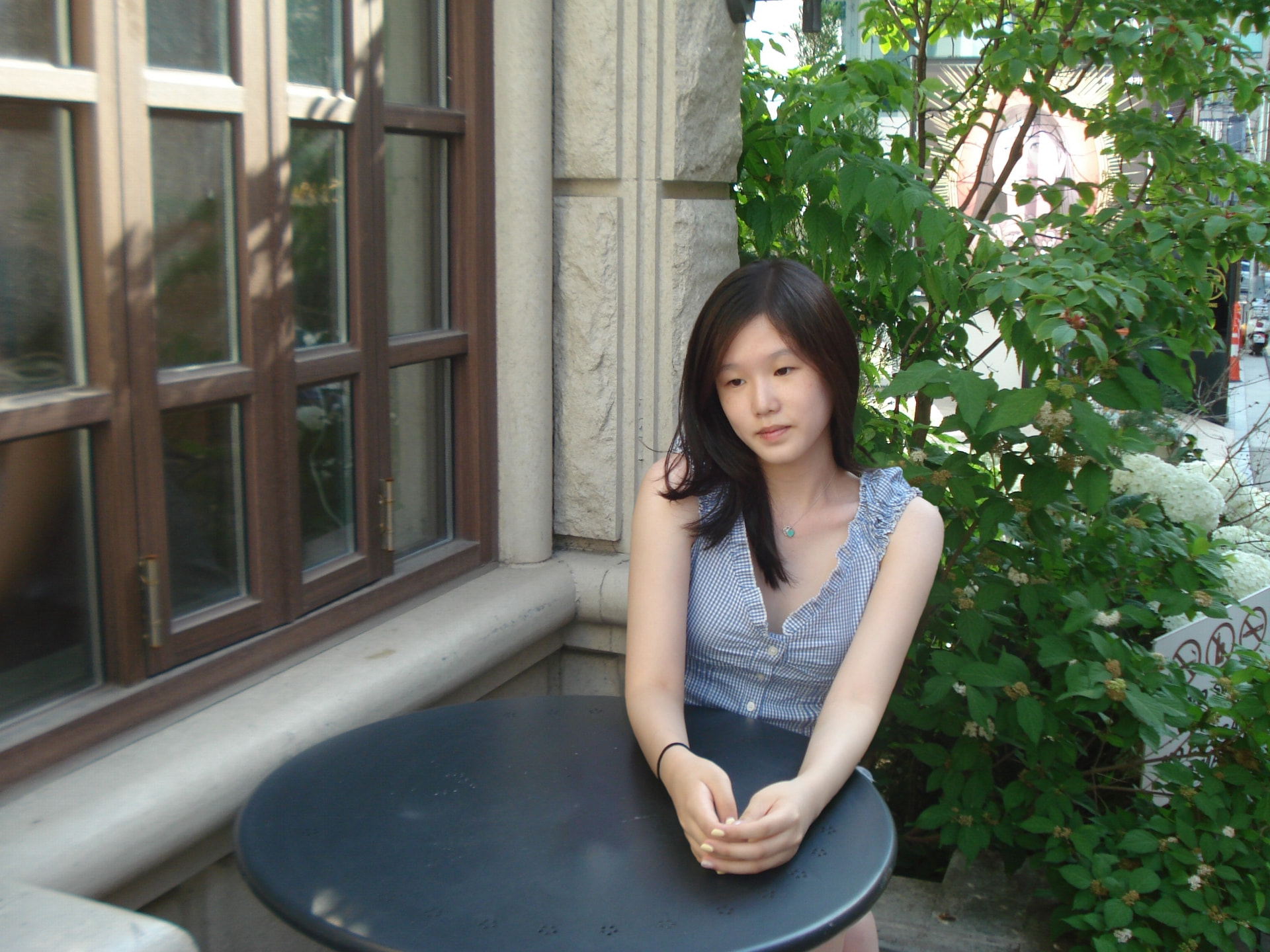 Siyeon Park seated at an outdoor café table beside a stone pillar and greenery